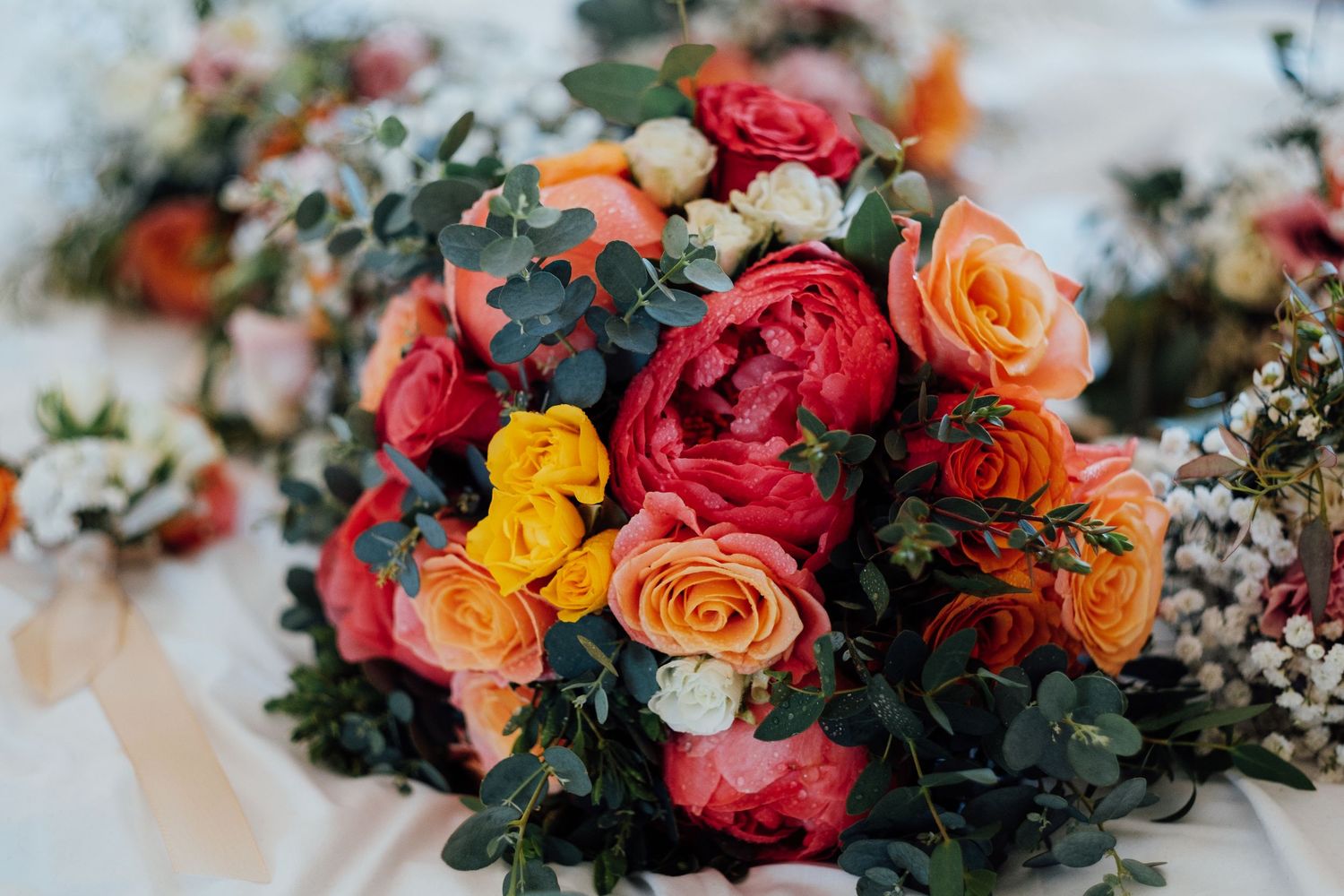 Vibrant wedding bouquet featuring red, orange, and yellow roses with mixed greenery.