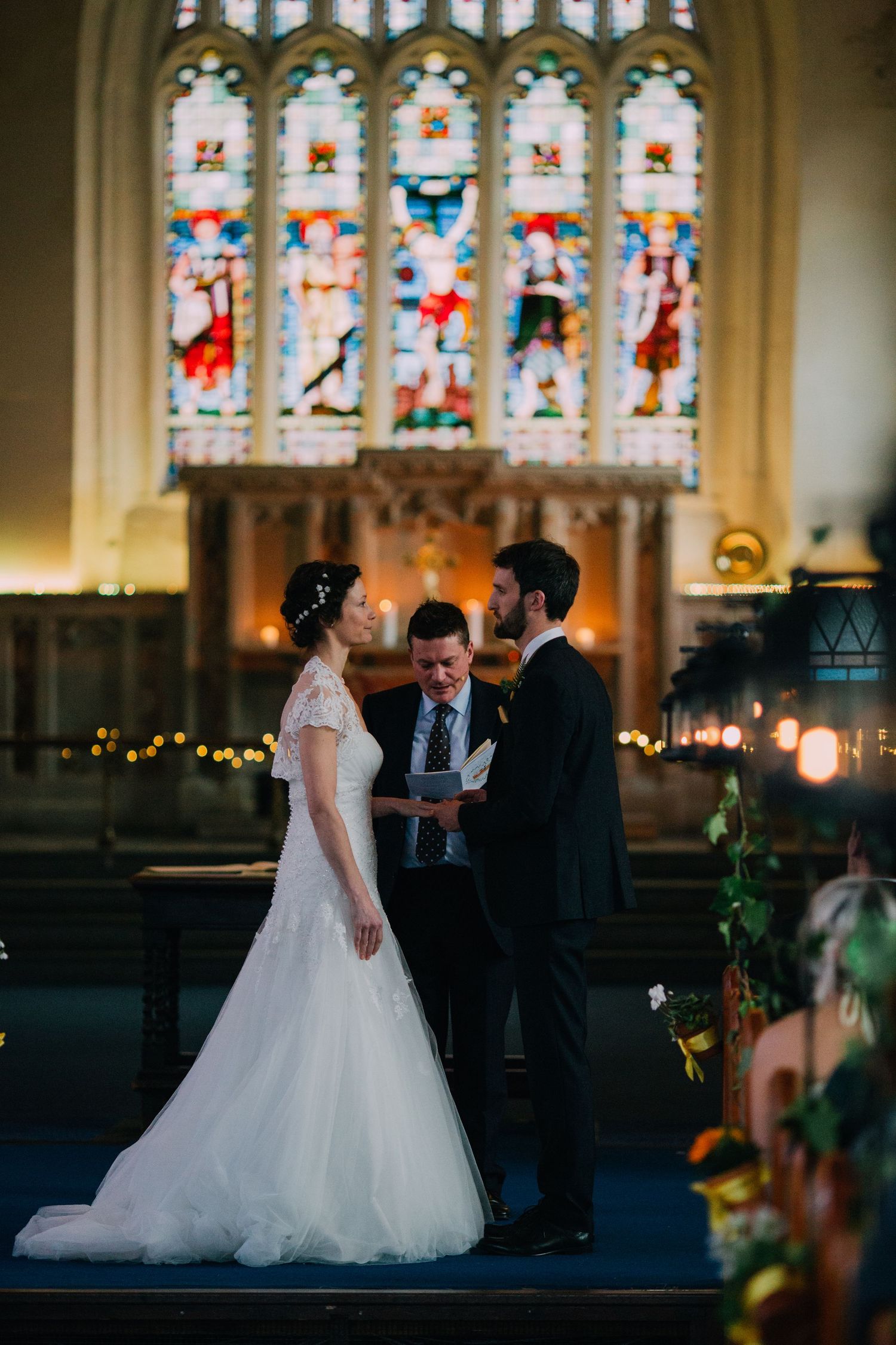 A wedding ceremony unfolds beneath a stunning stained glass window in a historic church.
