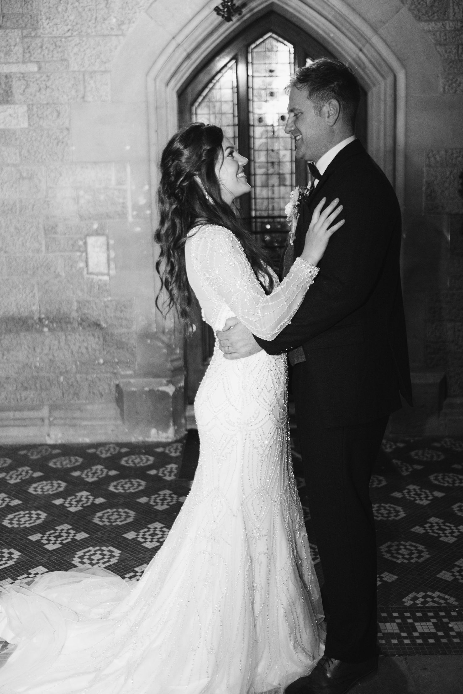 Black and white wedding portraits in historic stone hallway with arched windows.