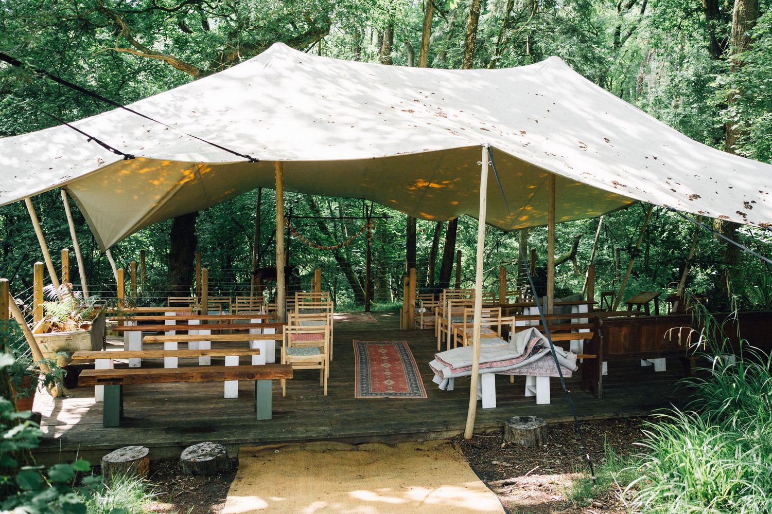 Canvas tent structures set up in a wooded area create an outdoor event space with natural surroundings.