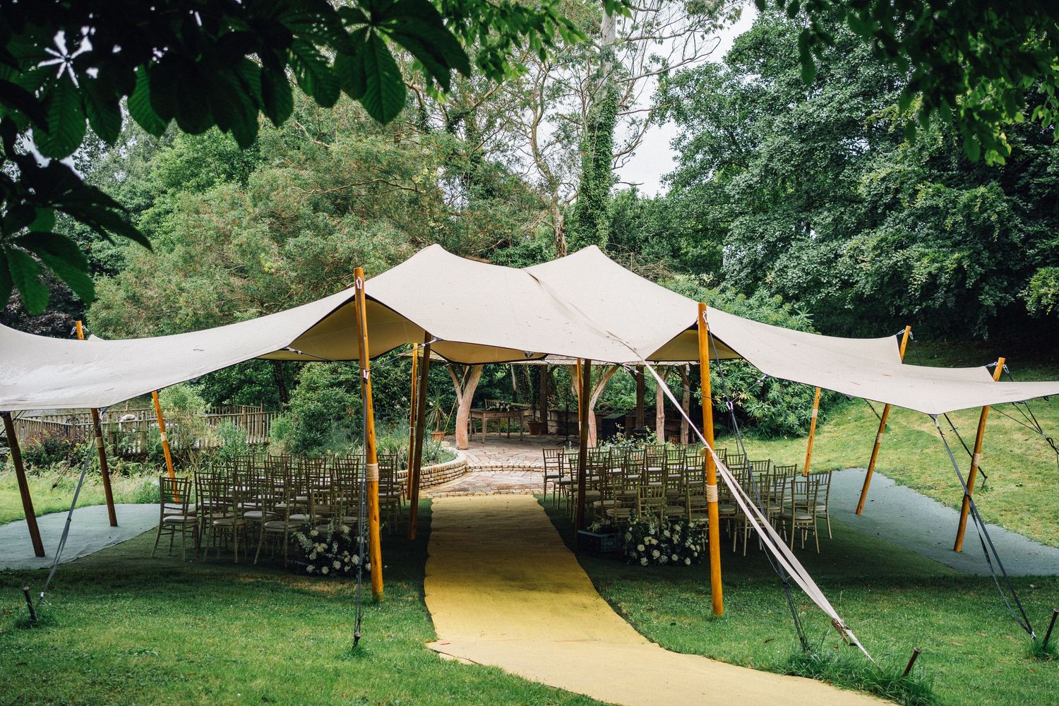 Elegant stretch tent canopy setup in a lush garden setting with white fabric and wooden poles creating an outdoor venue space.