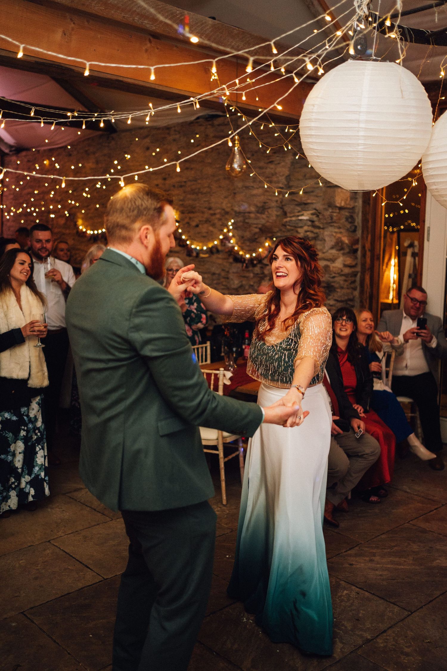 A couple shares a romantic dance at a rustic wedding reception decorated with twinkling string lights and paper lanterns.
