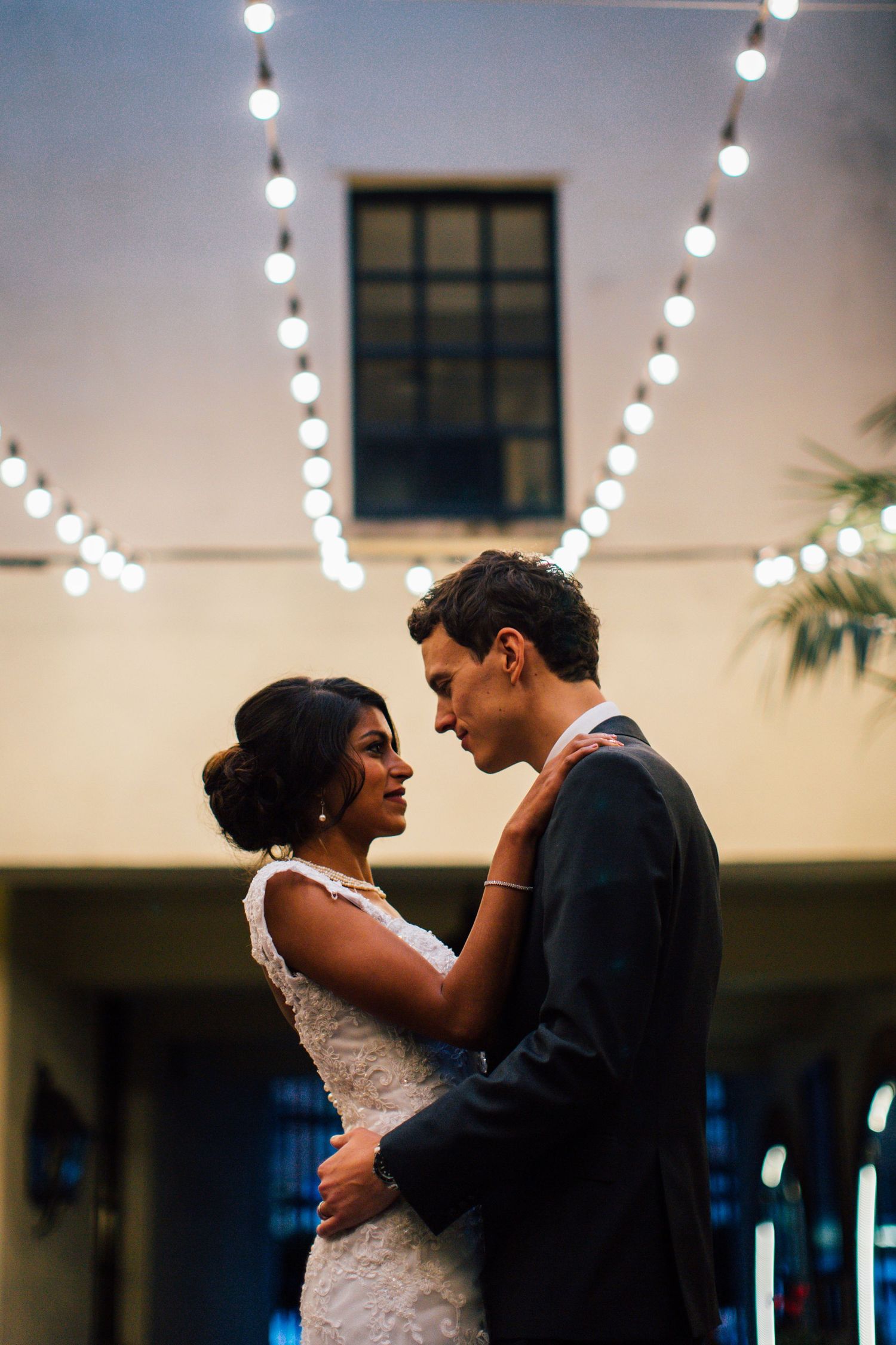 A romantic wedding dance scene illuminated by string lights in an elegant indoor venue.