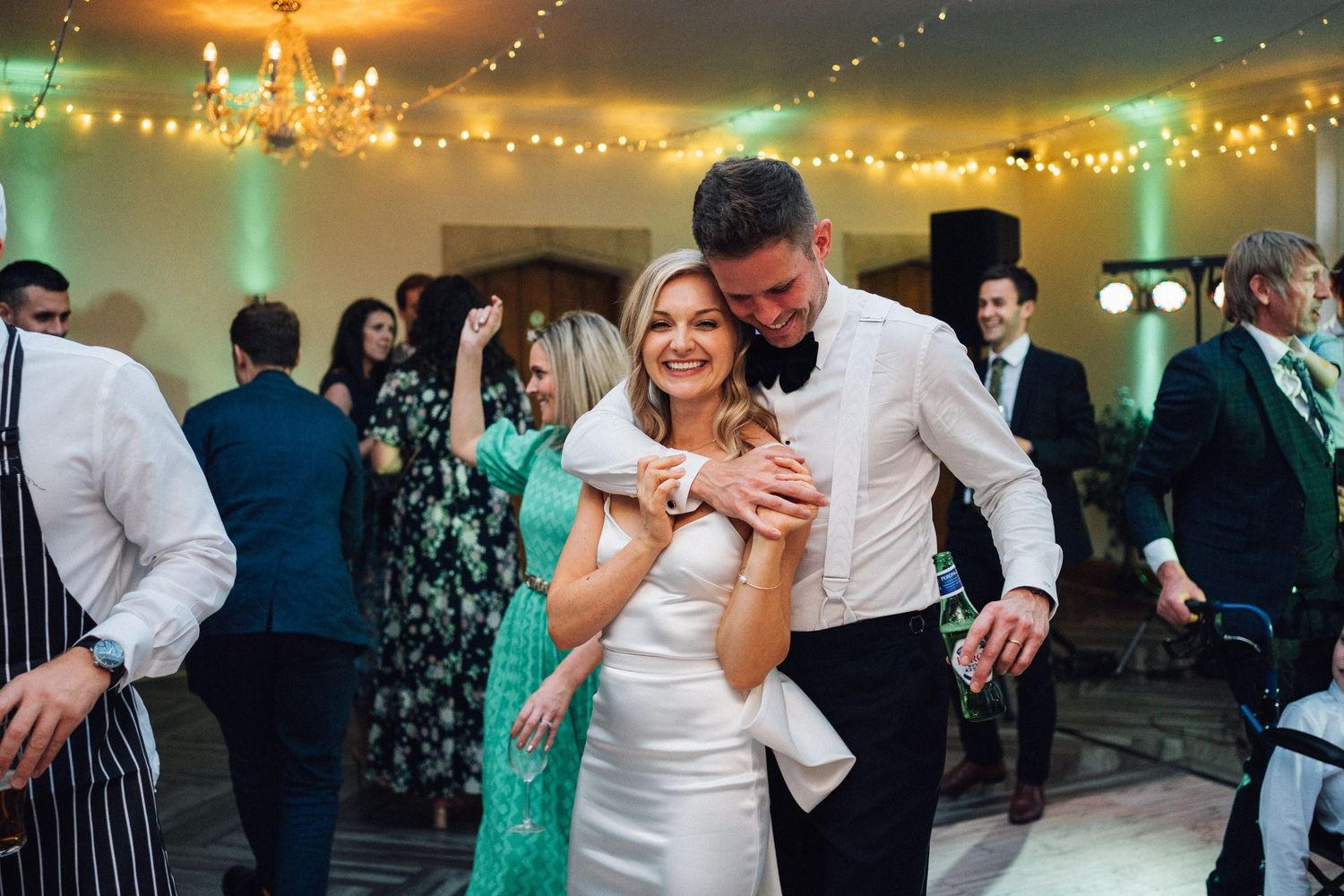 Wedding reception party with string lights overhead as guests dance and celebrate in an indoor venue.