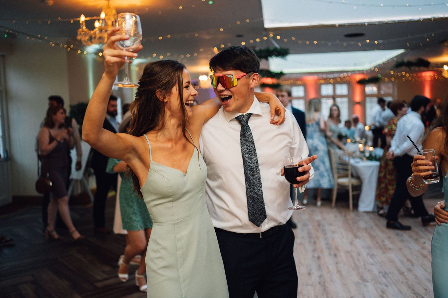 A couple dancing together at an indoor wedding reception with string lights overhead.