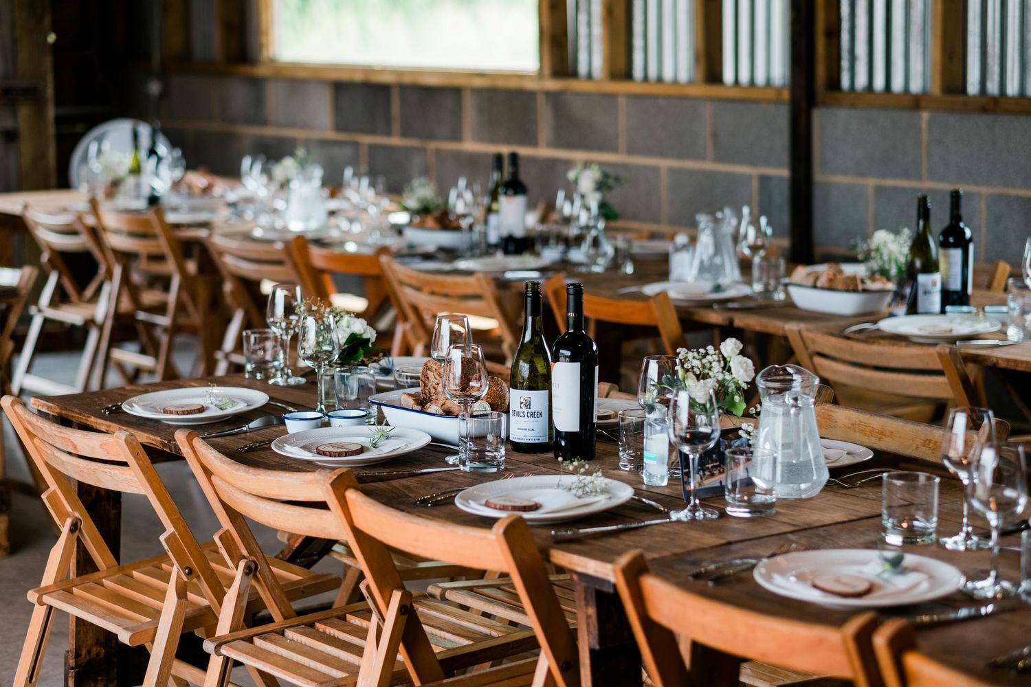 Rustic barn wedding reception venue with long wooden tables and elegant place settings.