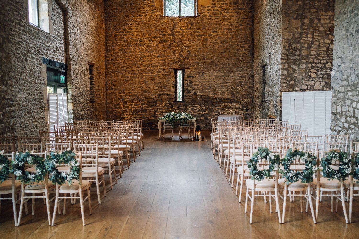 Elegant barn wedding ceremony setup with chiavari chairs, floral decorations, and rustic stone walls in a converted barn venue.