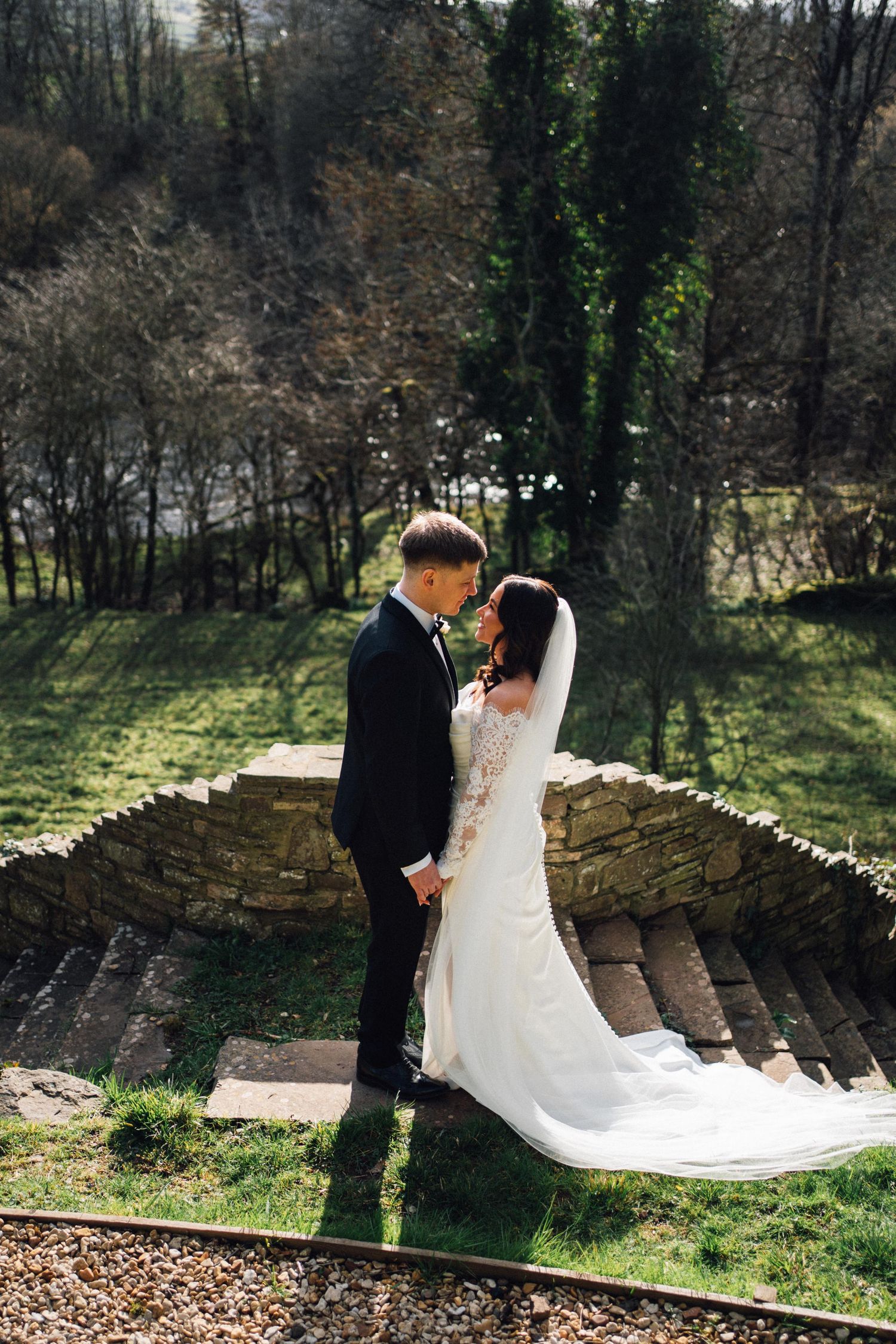 Bride and groom share a romantic moment on stone steps surrounded by lush greenery on their wedding day.