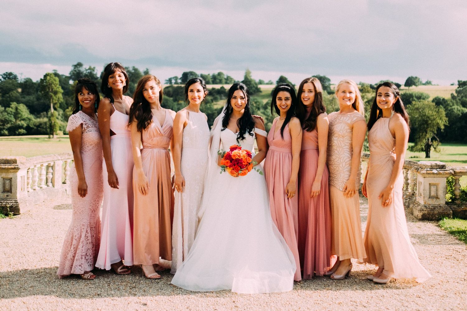 Wedding party in pink and peach dresses posed together on mansion grounds.