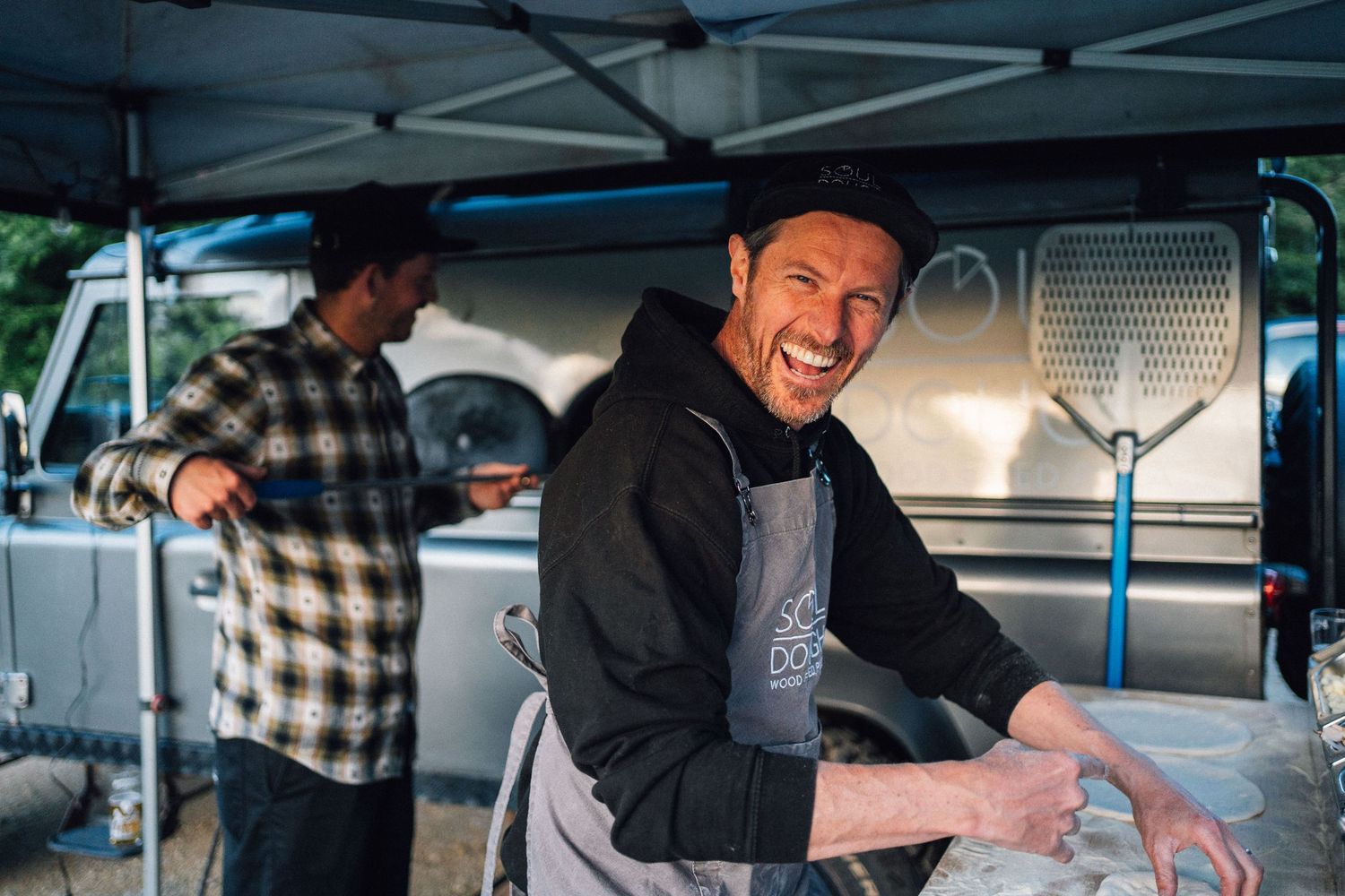 Food service workers in casual attire preparing food at an outdoor station.