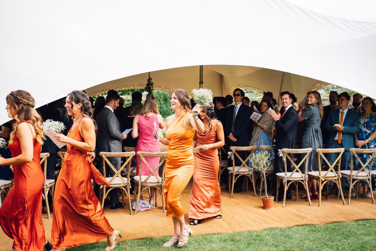 Bridesmaids in bright orange dresses dance in formation during wedding reception festivities.