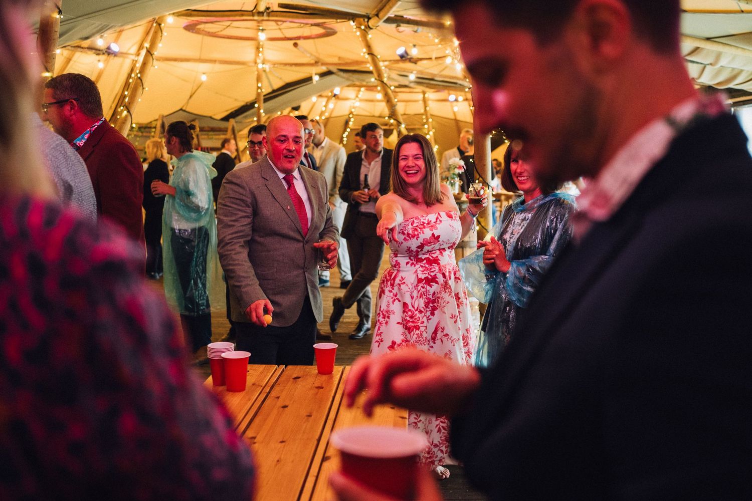 Wedding reception guests dancing and celebrating inside a warmly lit tent venue.