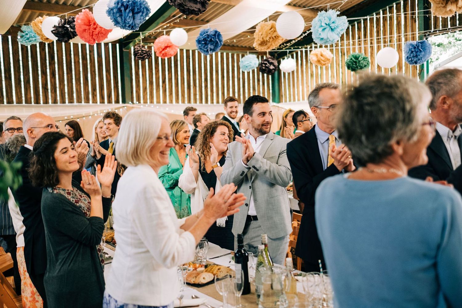 Festive party decorations including colorful paper poms hang above dining tables at a celebration.