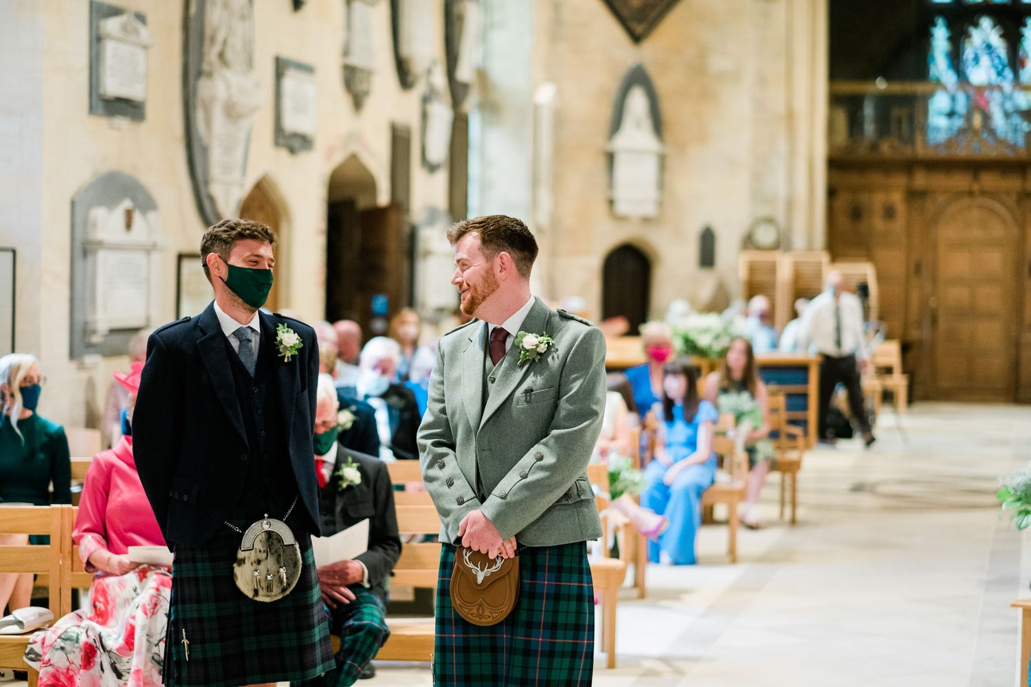 Two men in traditional Scottish kilts standing in historic church interior.