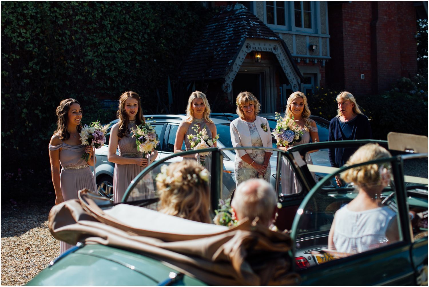 Wedding party gathered around a classic green convertible car outdoors.