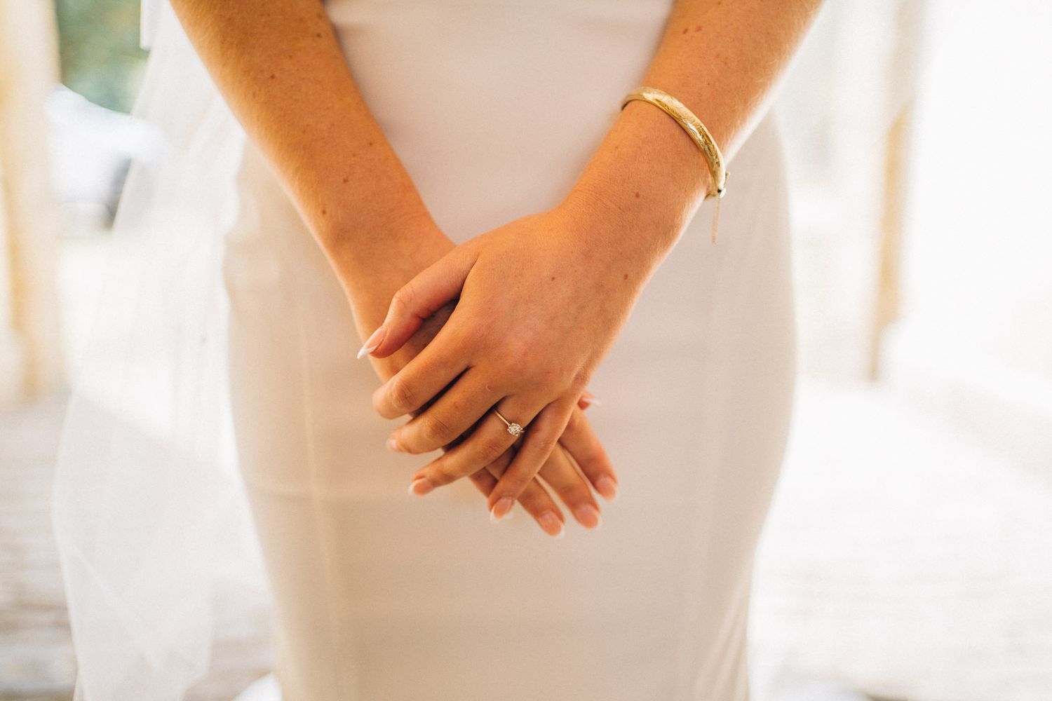 Close-up of clasped hands showing delicate jewelry against a white wedding dress.
