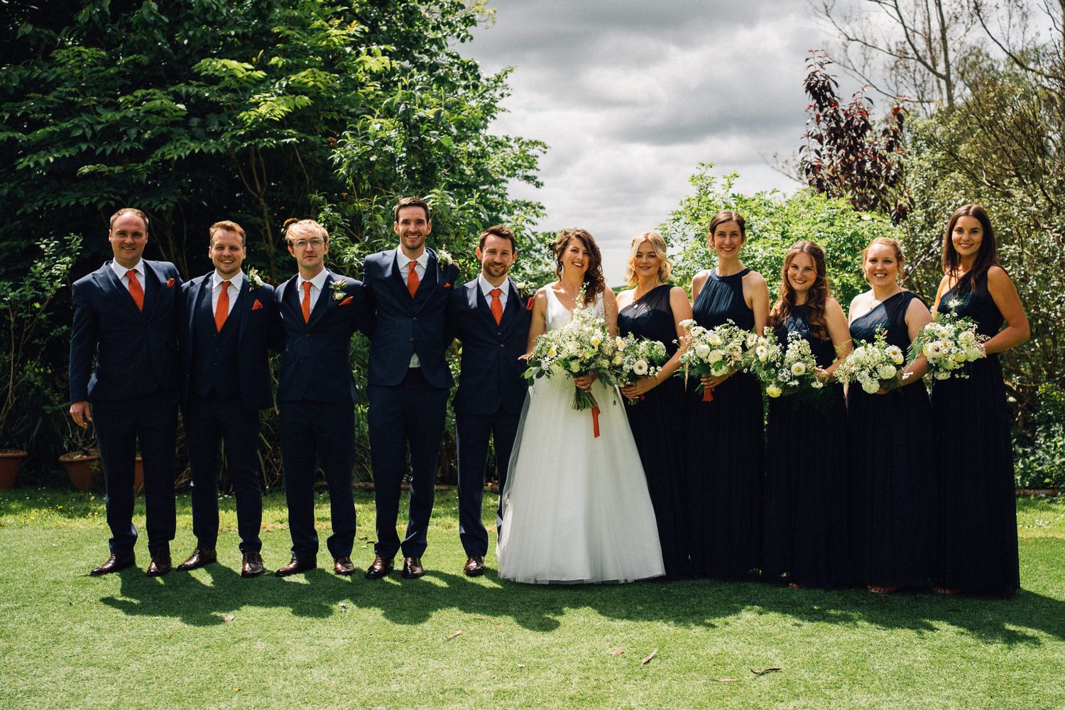 Large wedding party group photo taken outdoors on a cloudy summer day.