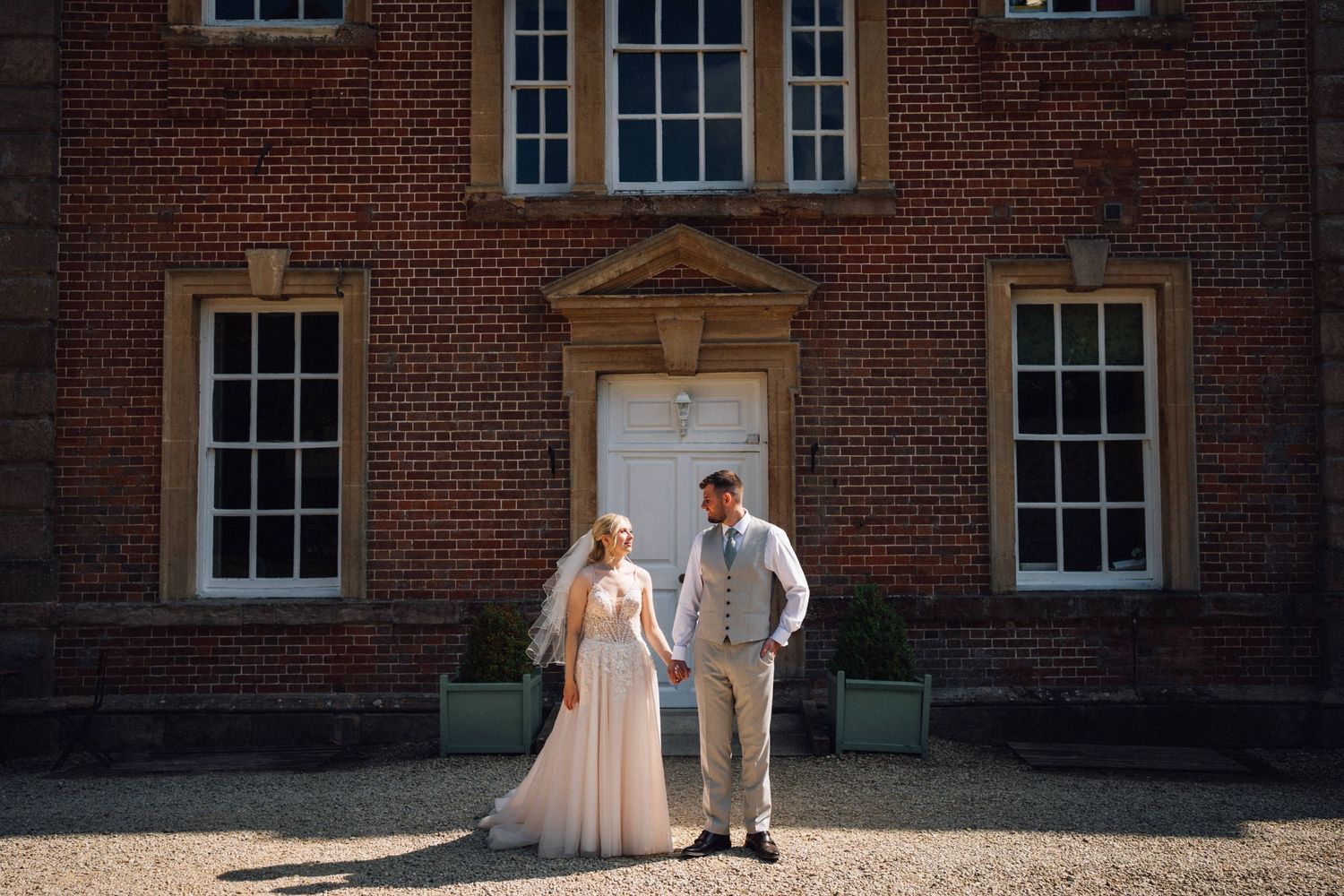 A couple poses together outside a historic brick building on their wedding day.