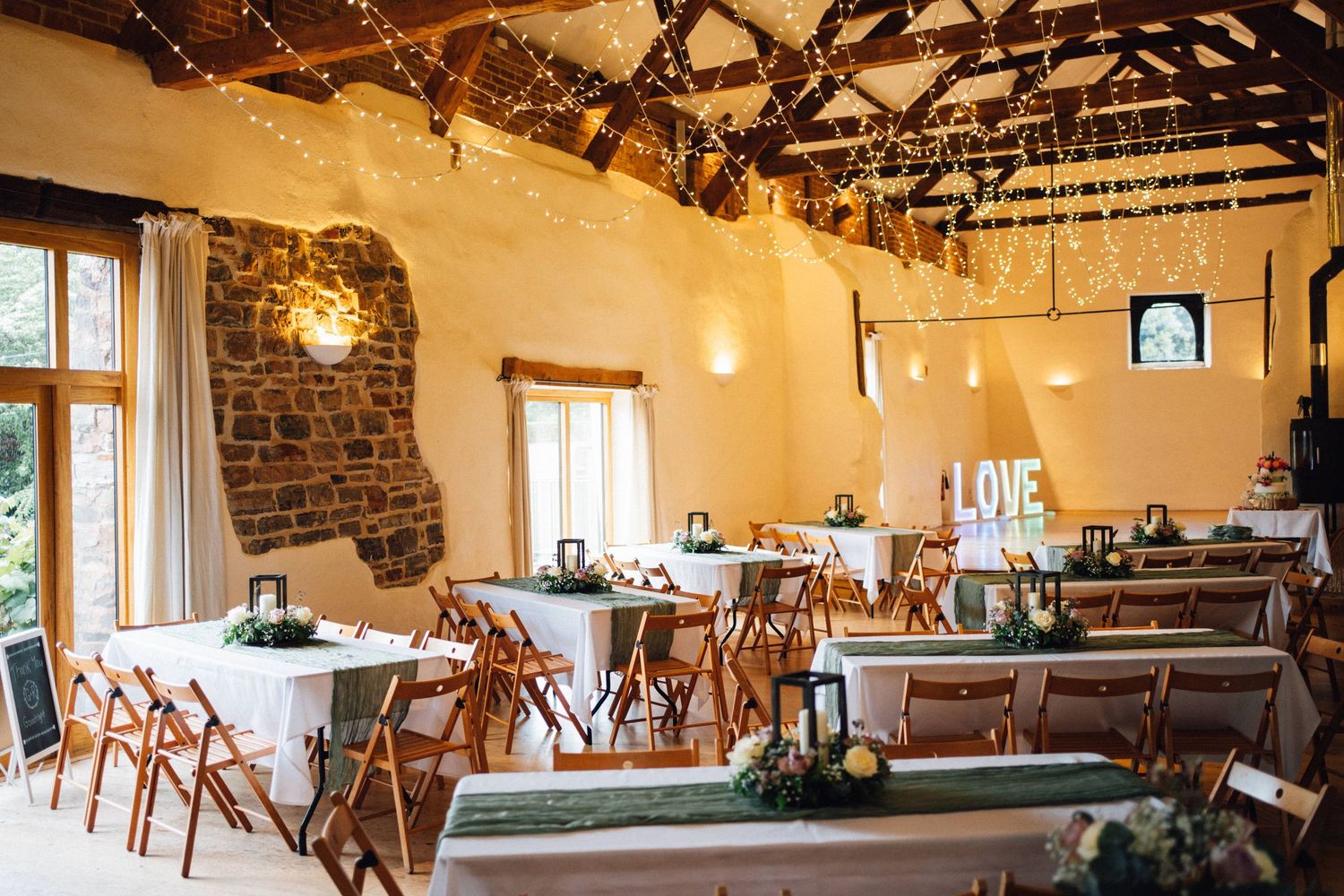 Rustic wedding reception venue with exposed wooden beams, stone walls, and string lights creating a warm atmosphere.