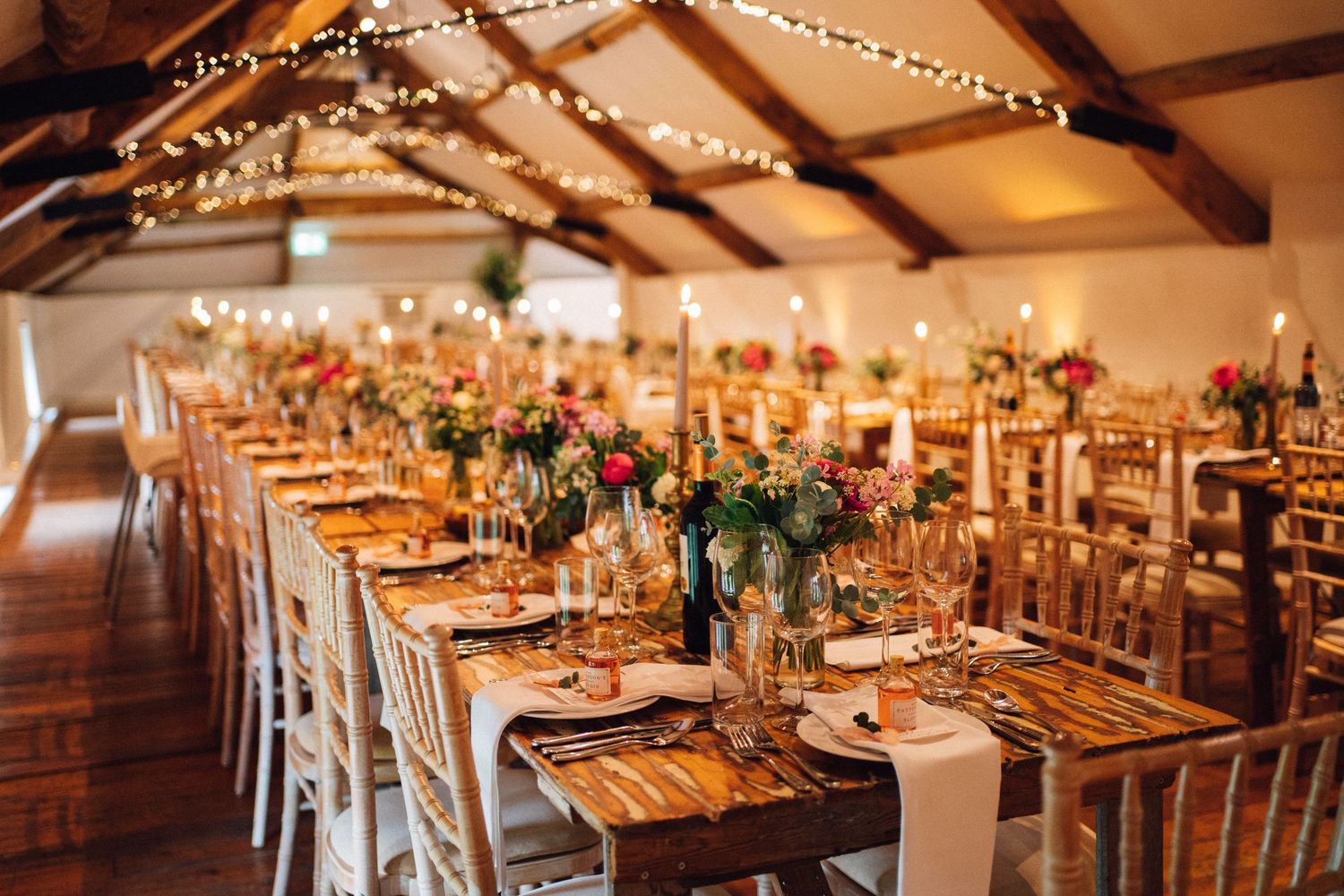 Wedding reception tables decorated with floral centerpieces and candles in a rustic barn setting.