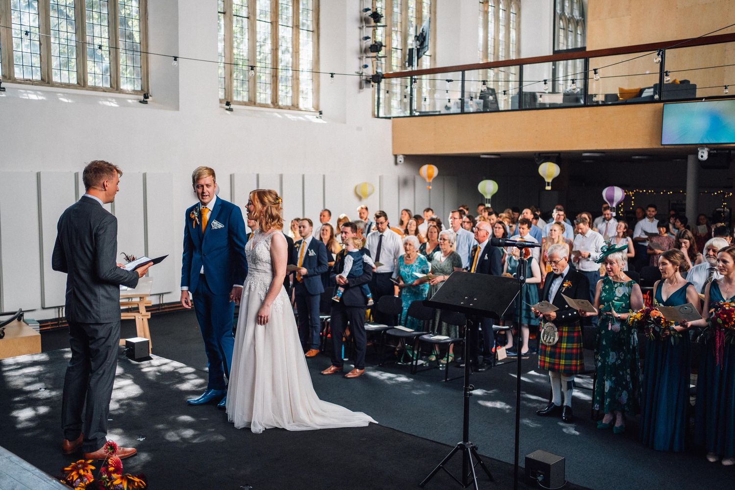 Wedding ceremony setup in a bright indoor venue with white chairs and natural lighting streaming through windows.