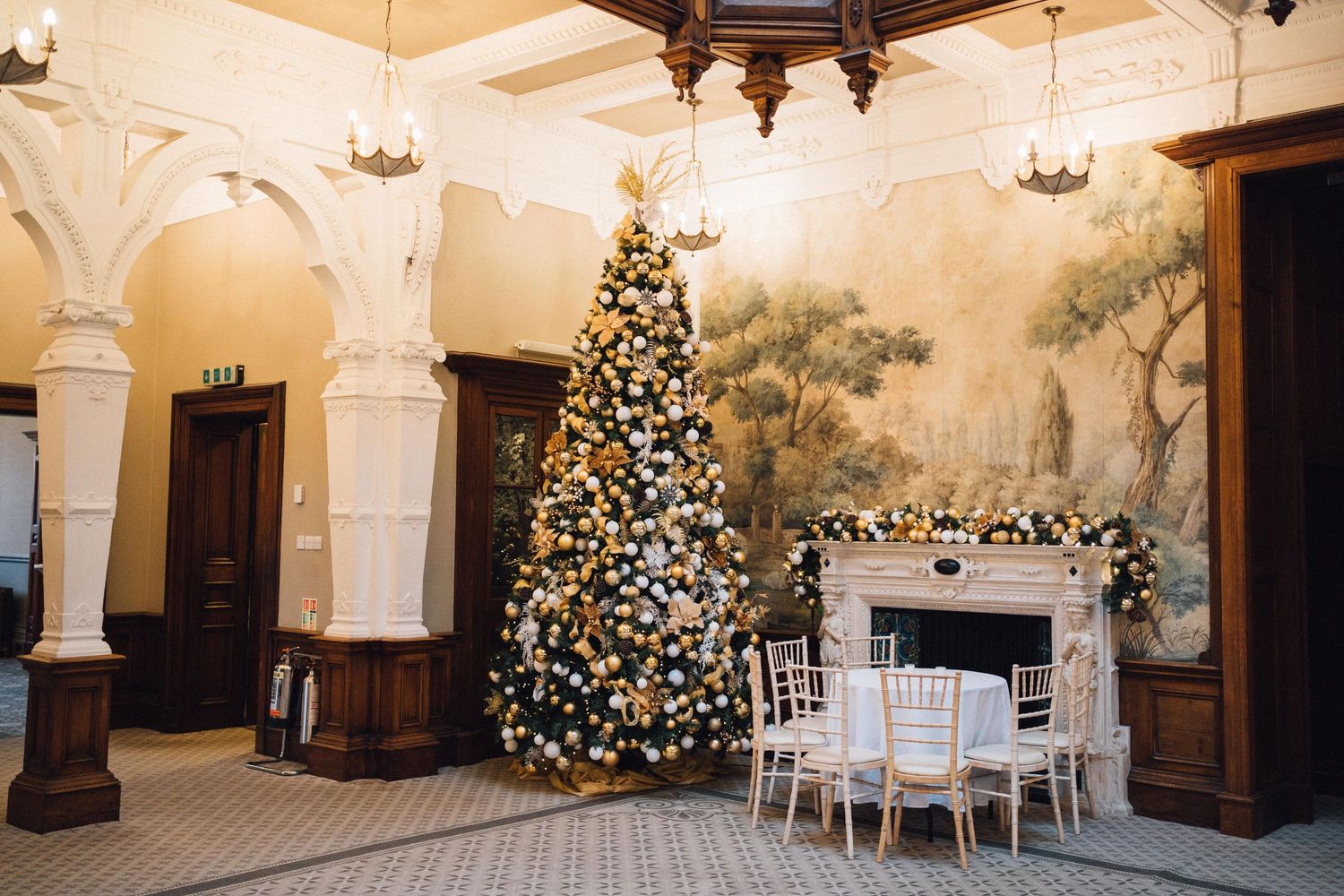 Elegant indoor venue space decorated with Christmas trees, white columns, and crystal chandeliers.