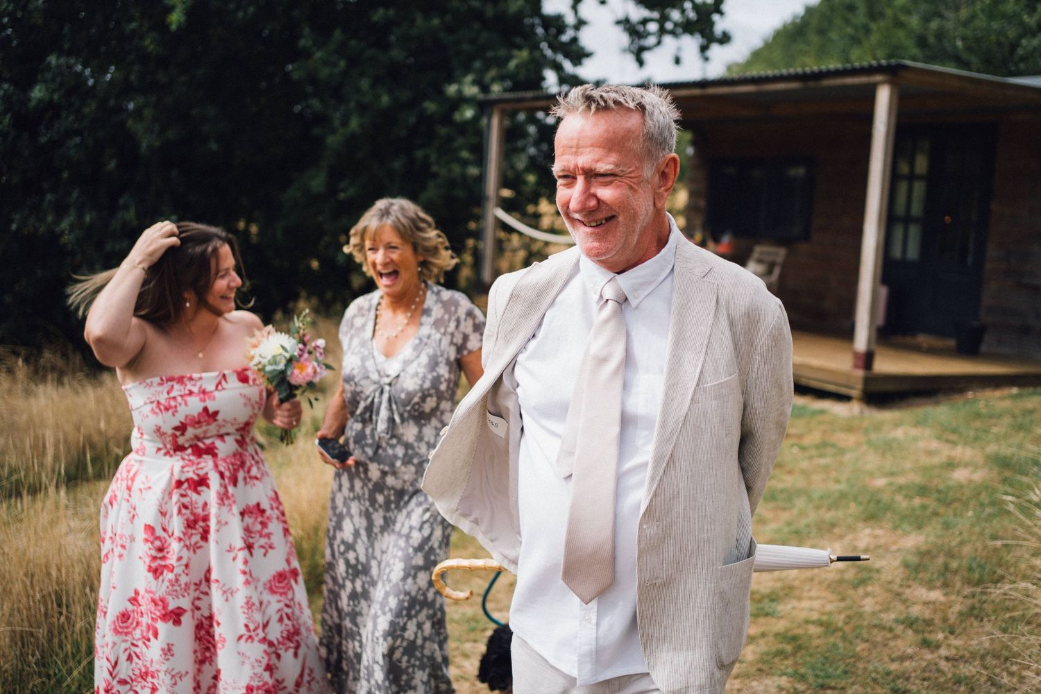 Wedding guests share a joyful moment outdoors with floral dresses and light summer attire.