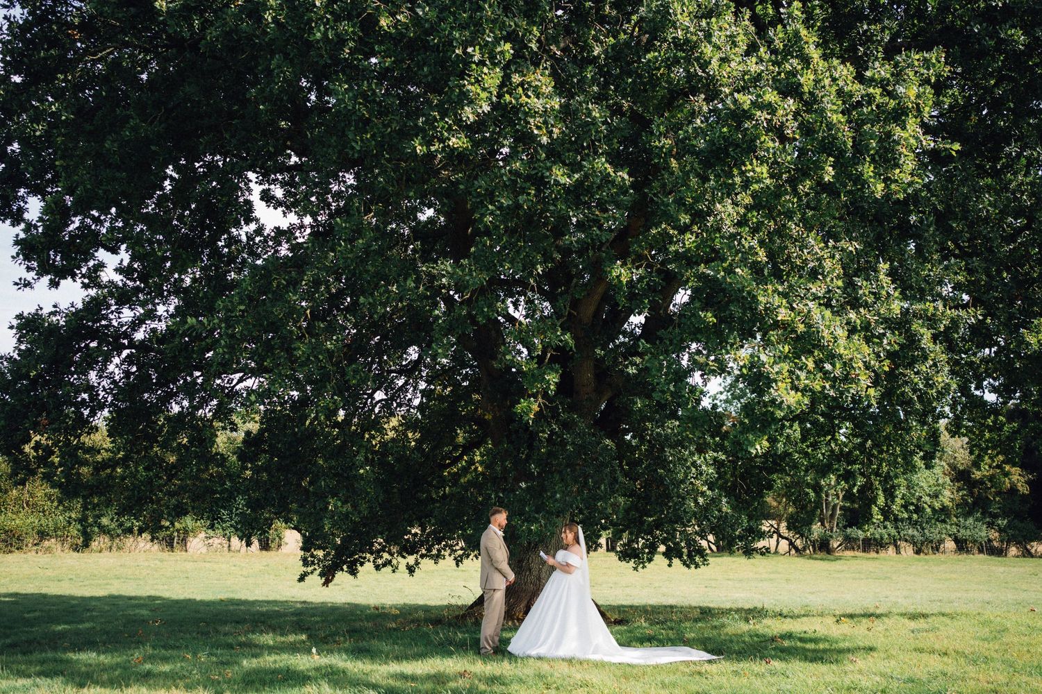 A scenic outdoor wedding venue with lush green trees and a white teepee tent set up on a grassy field in the chew valley.