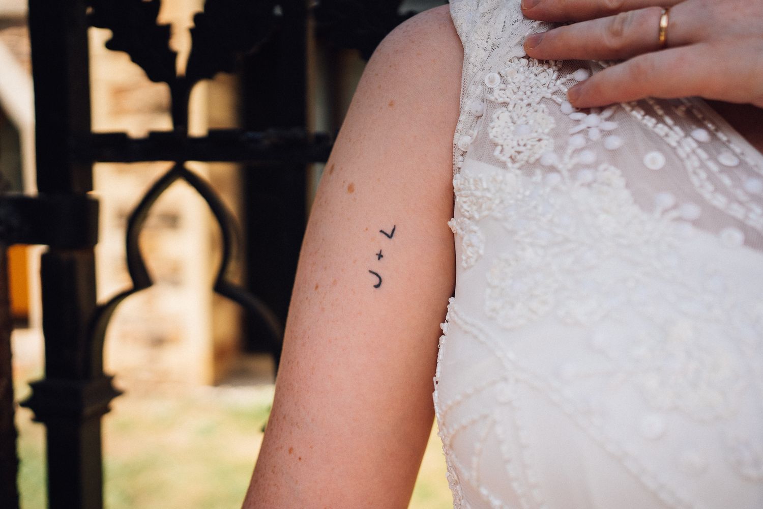 Close-up detail of a small tattoo on an arm against white lace wedding dress fabric.