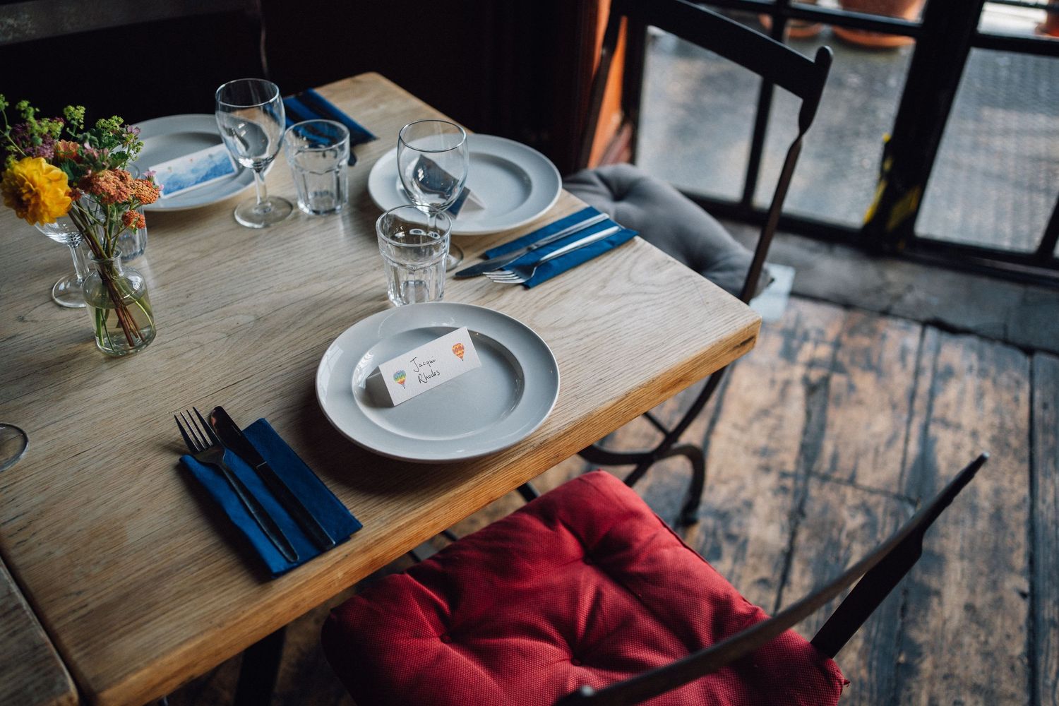 Rustic wooden dining tables set with wine glasses and blue napkins in a restaurant interior.