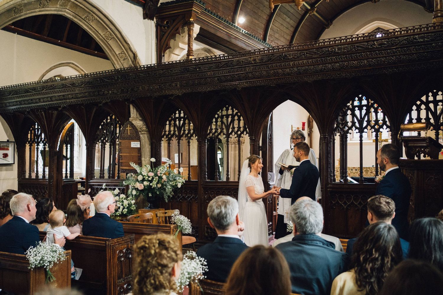 Traditional church wedding ceremony with ornate wooden screens and floral decorations.