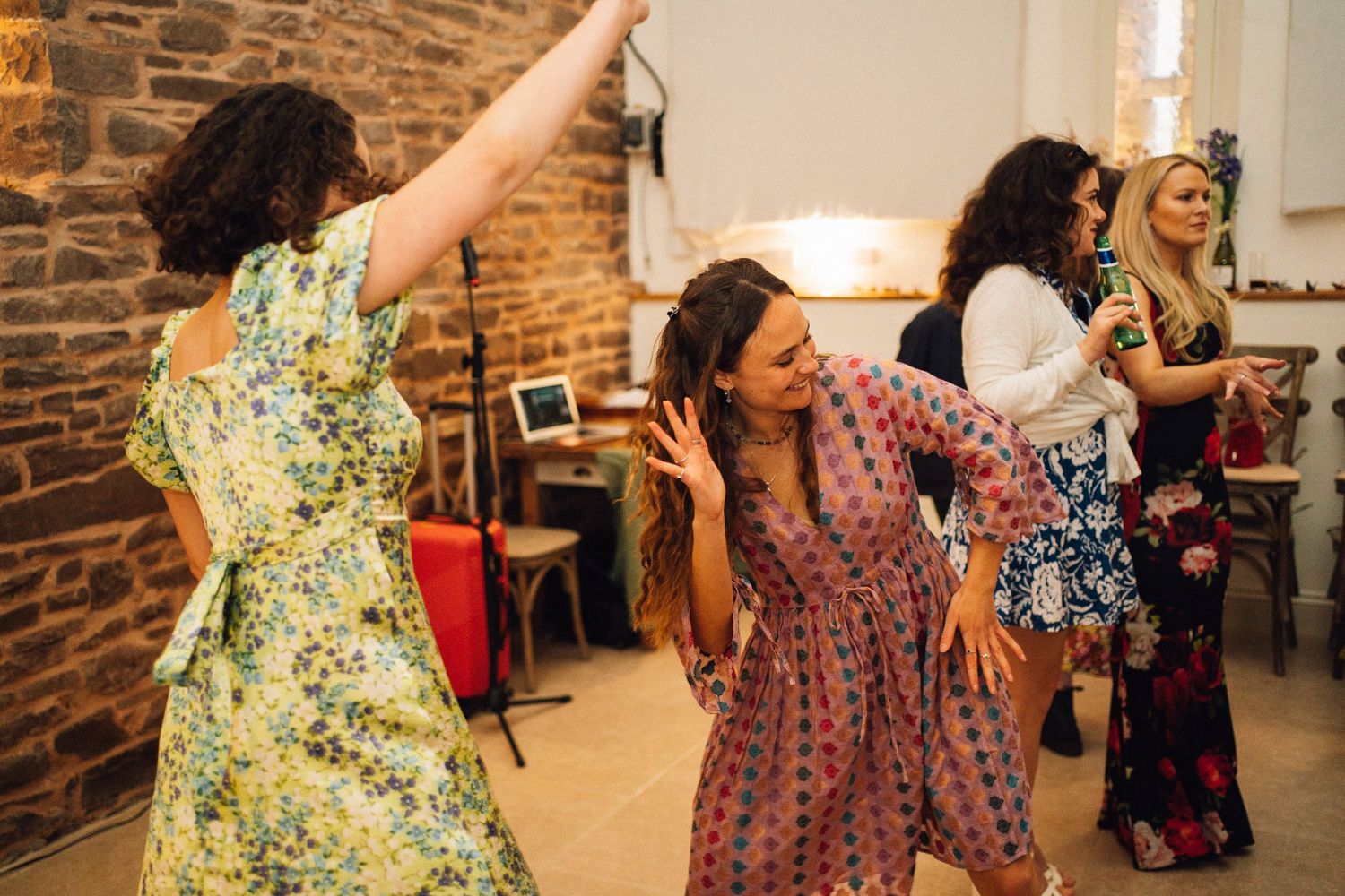 Group of people dancing joyfully in floral dresses at indoor celebration.