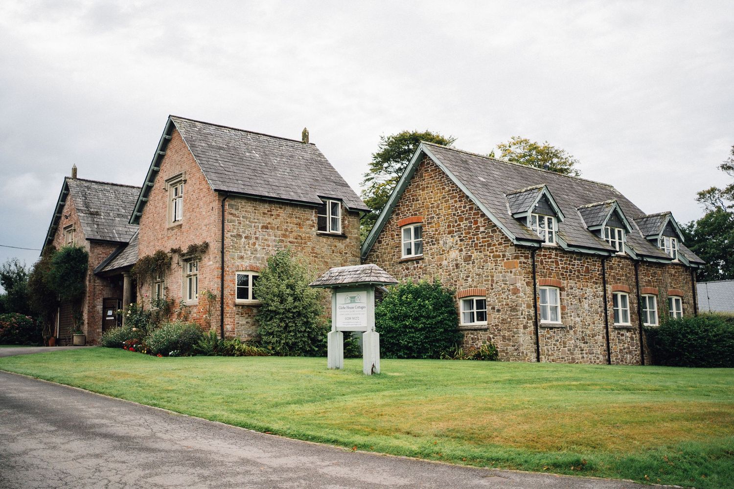 Two rustic stone country houses with dormer windows and green lawns stand side by side on a rural property.
