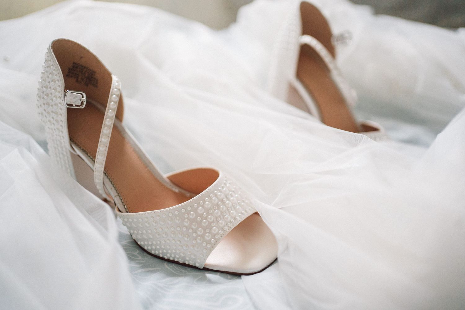 Elegant white lace bridal flats with peep toe design resting on delicate tulle fabric.