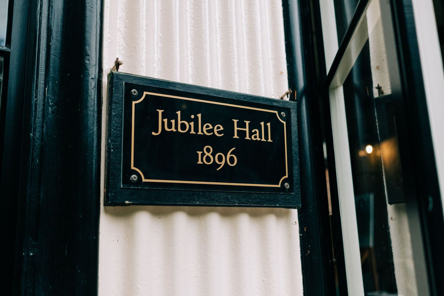 Black and gold vintage sign reading 'Jubilee Hall 1896' mounted on a dark wall.