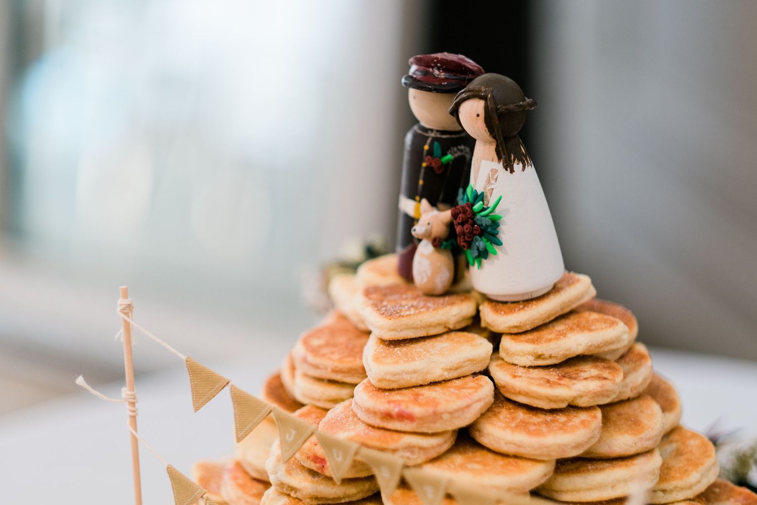 Rustic display of mini pancakes stacked on a wooden slice platter with decorative garnishes.