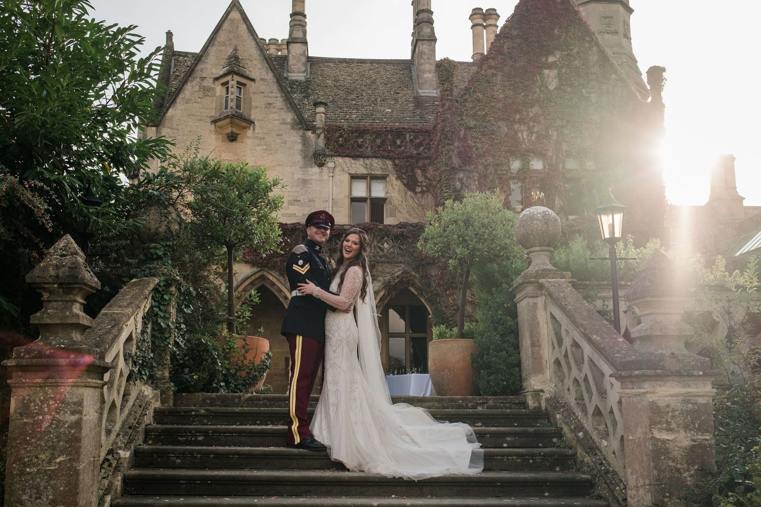 Wedding couple on stone steps of a historic manor house at sunset.