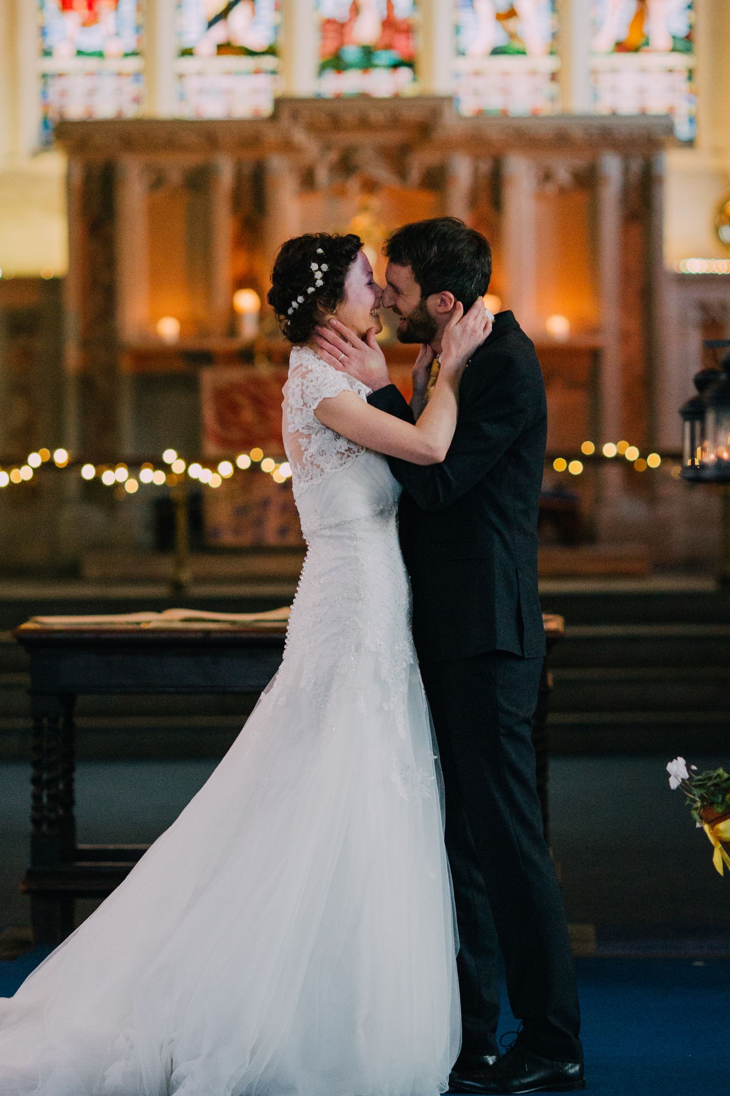 An intimate wedding moment in a church with decorative string lights and stained glass windows.