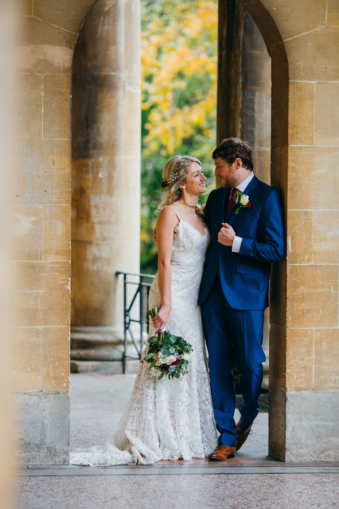 A couple shares an intimate moment beneath a colonnade of stone pillars.