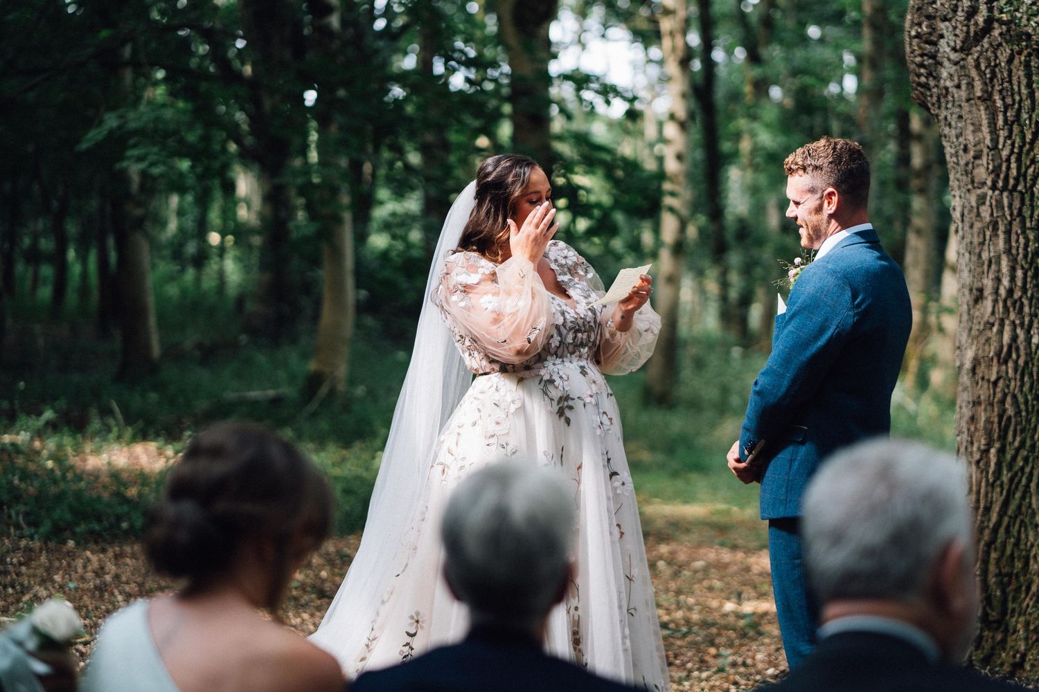 An intimate forest wedding ceremony with guests watching under a canopy of trees.