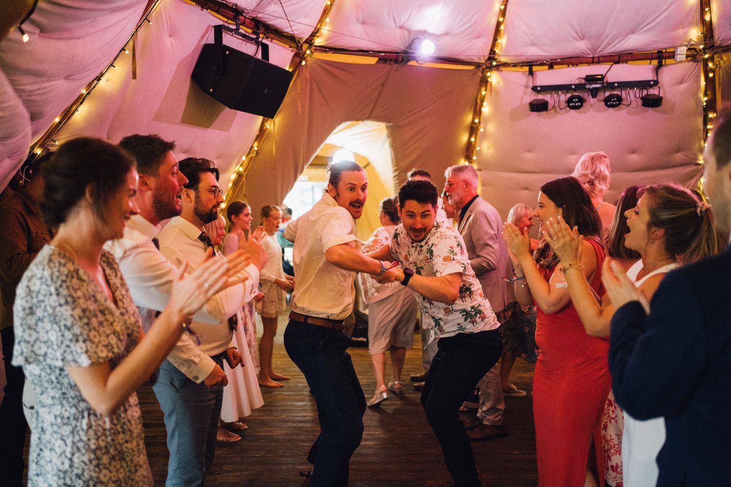 People dancing and celebrating under string lights in a tent venue.
