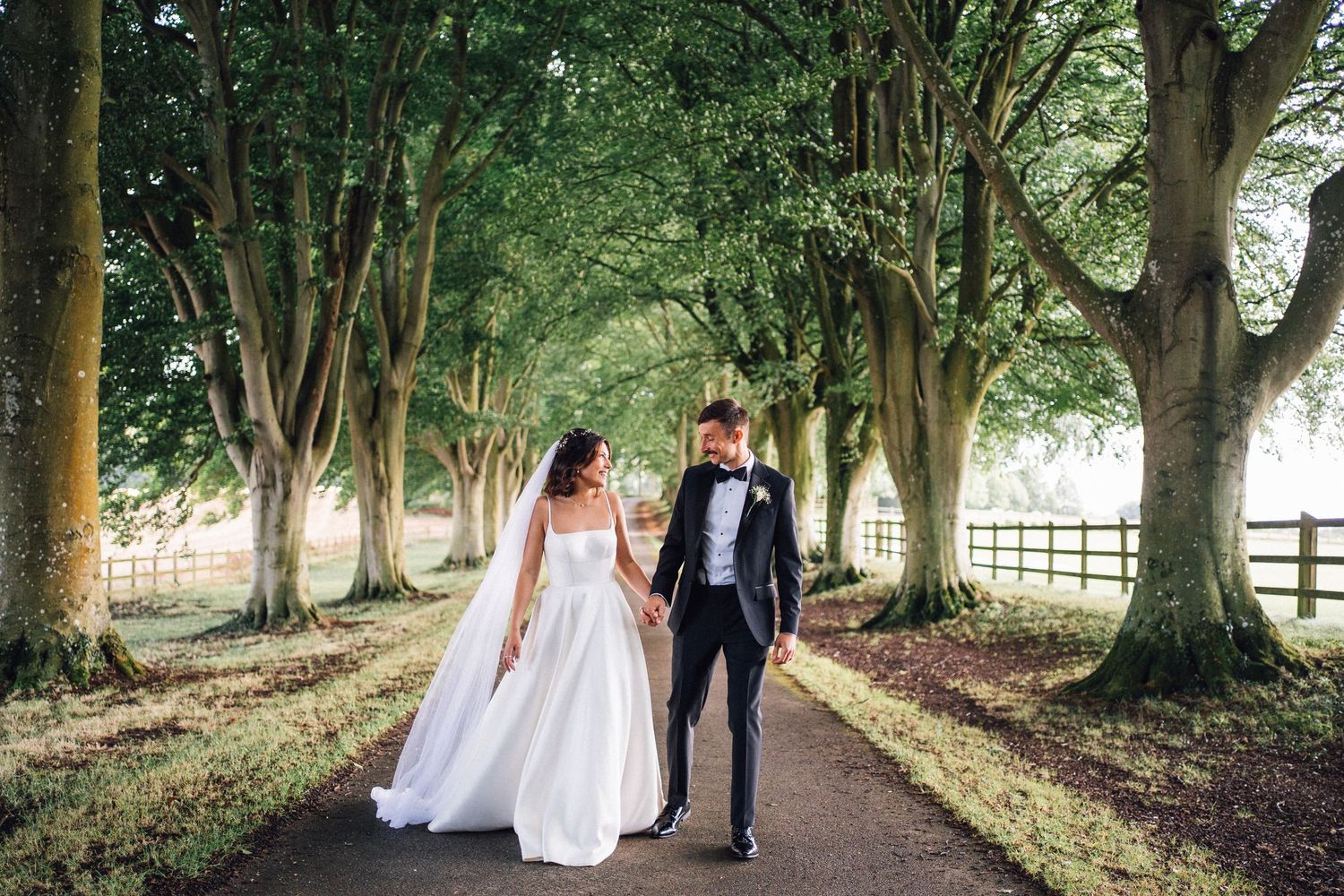 Wedding couple strolls down a scenic tree-lined path on their special day.