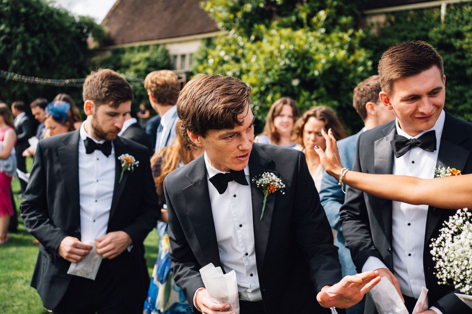 Wedding party members in formal attire celebrate with confetti under an outdoor tent.