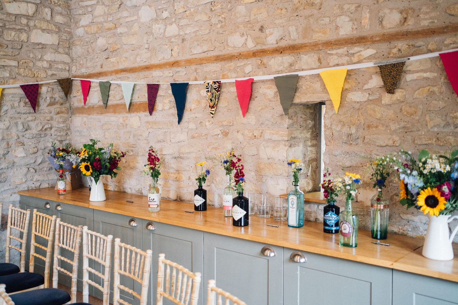 Stone wall wedding venue decorated with floral centerpieces, bunting flags and wooden tables.