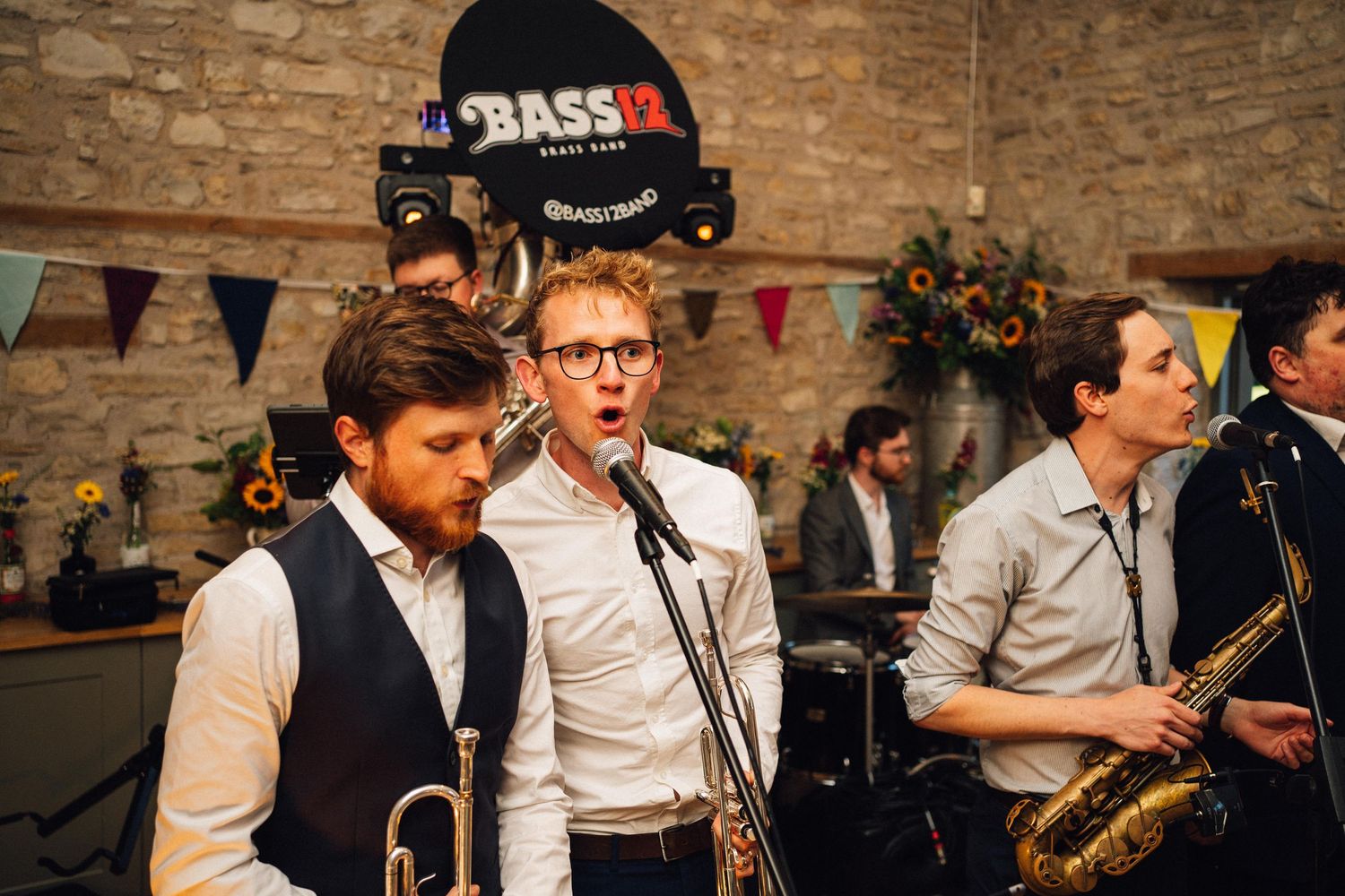 Brass band members performing energetically at a wedding reception with colorful bunting overhead.
