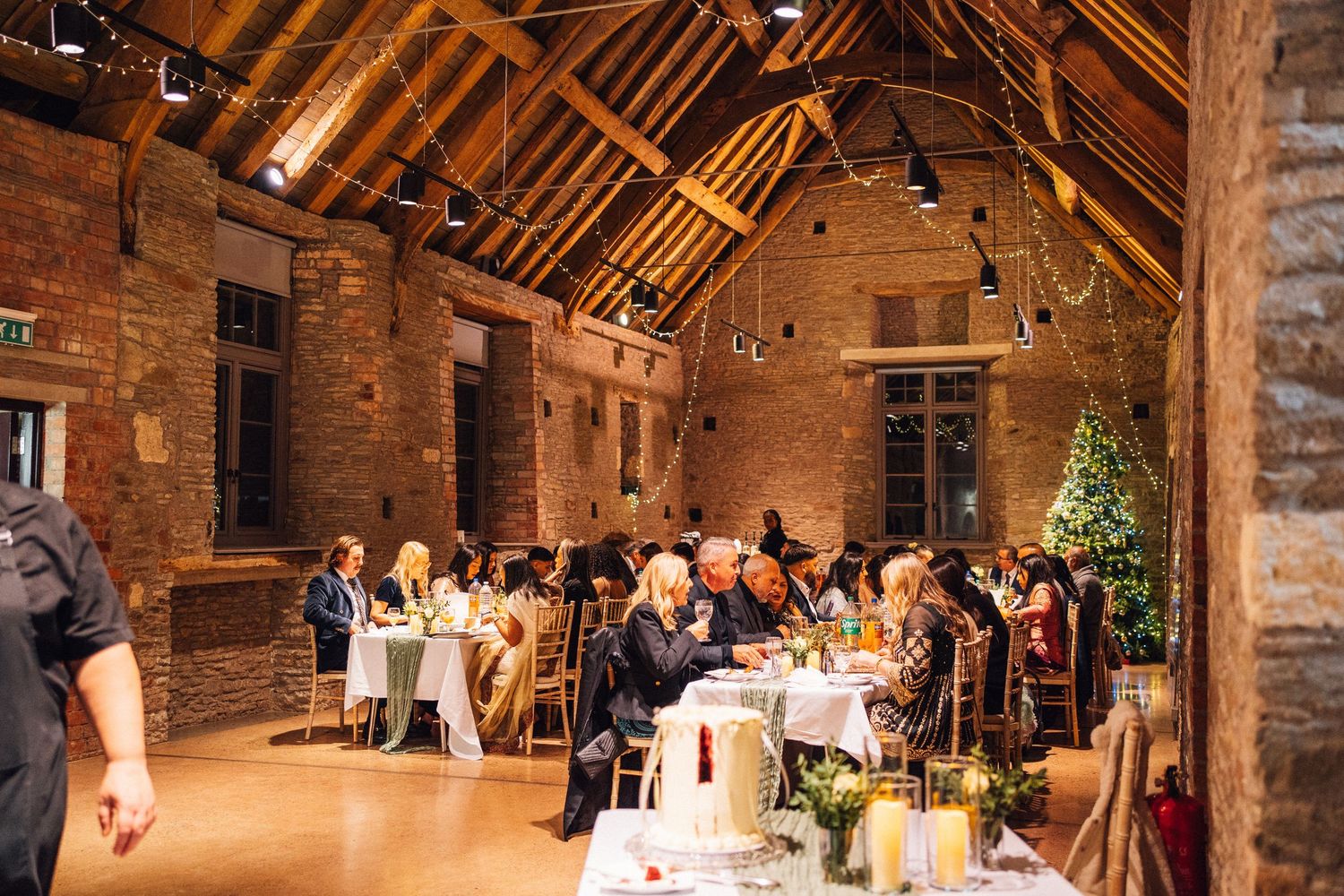 Panoramic view of a barn wedding reception with wooden beams, brick walls and elegant table settings.