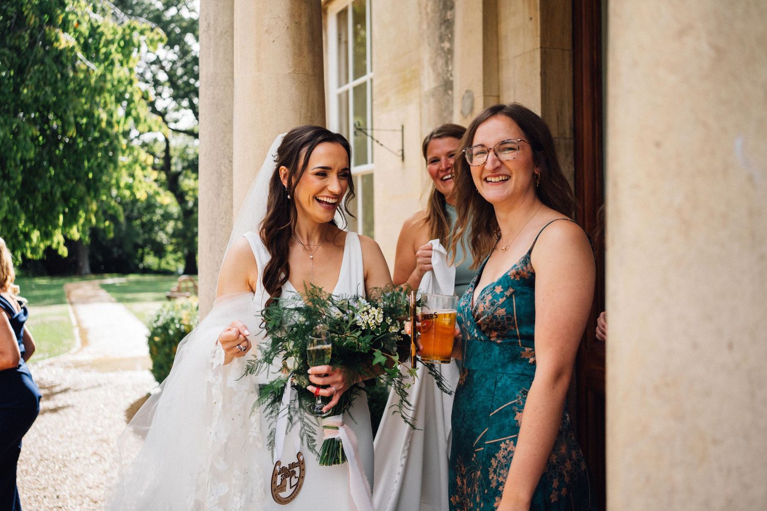 Bridesmaids in light colored dresses gathered outside on a covered porch.