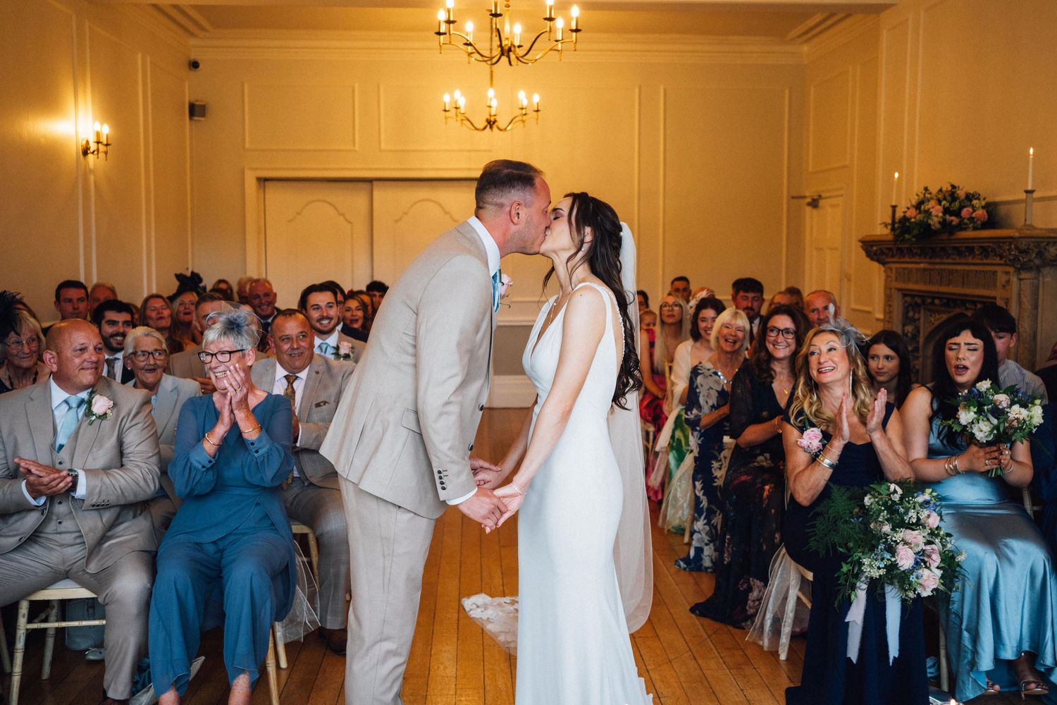 Wedding guests celebrate and dance together during a joyous reception in an elegant ballroom with chandeliers.