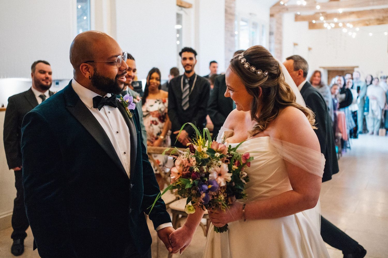 Bride and groom share their first dance surrounded by wedding guests in a bright reception hall.