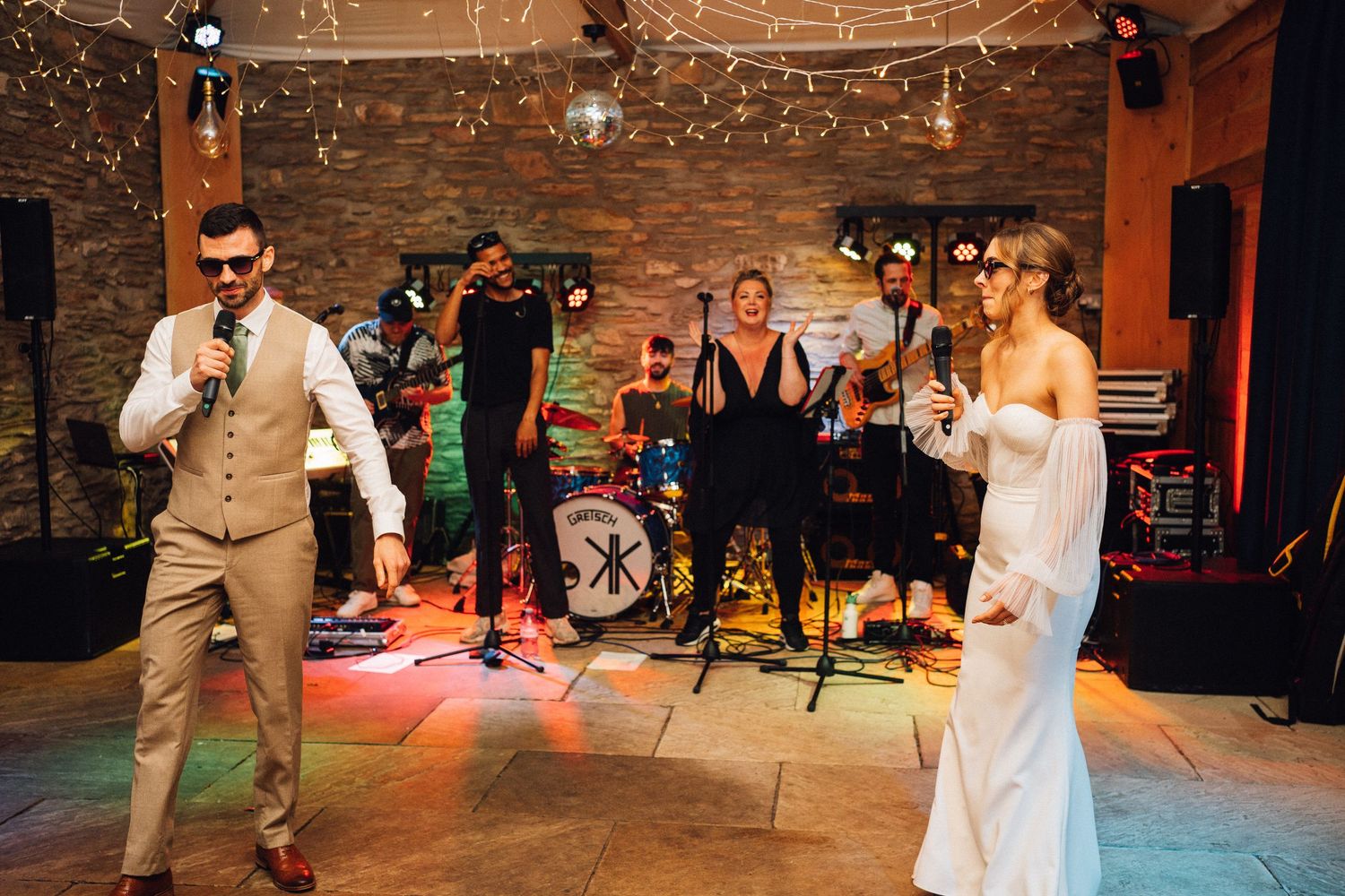 Wedding celebration on dance floor with string lights and rustic stone walls.